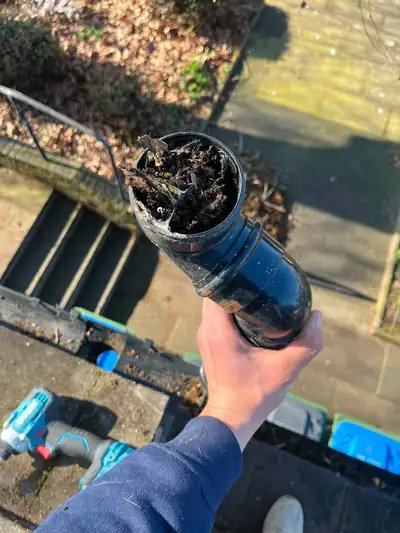 Section of downpipe held up to show it packed solid with moss and debris