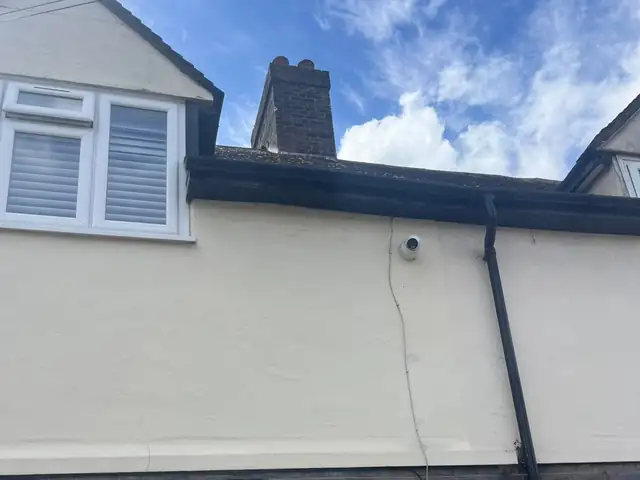 Rear of a rendered house with a leaking gutter and downpipe below the roof line, before the repair