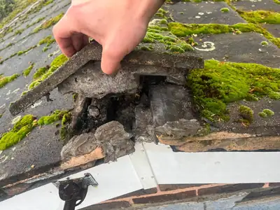 Damaged roof tile lifted to reveal crumbling bedding underneath