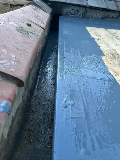 Reinforced fibreglass joint coated in grey liquid rubber where a flat roof meets a parapet wall
