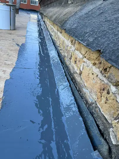 Grey liquid rubber coating applied along a flat roof upstand