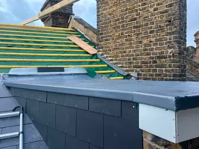 New battens on a slate roof beside a chimney stack, with a grey liquid rubber coated flat section in front